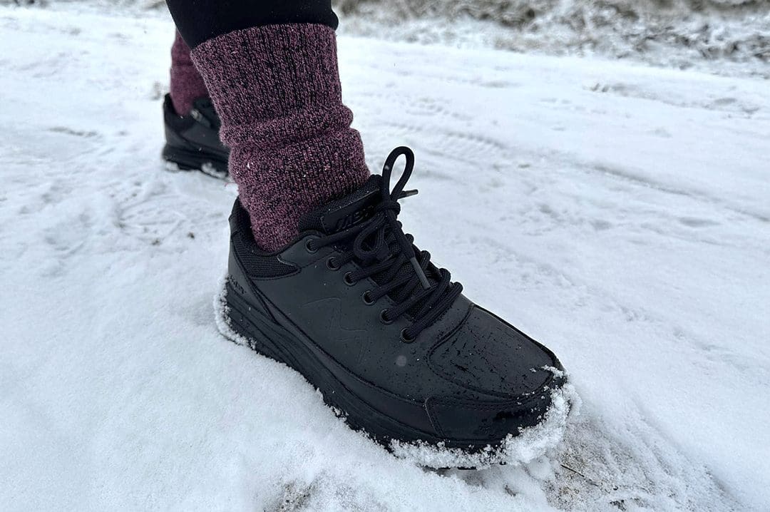Sort MBT Simba Trainer II Black damesko i hvid sne med varme lilla uldsokker.